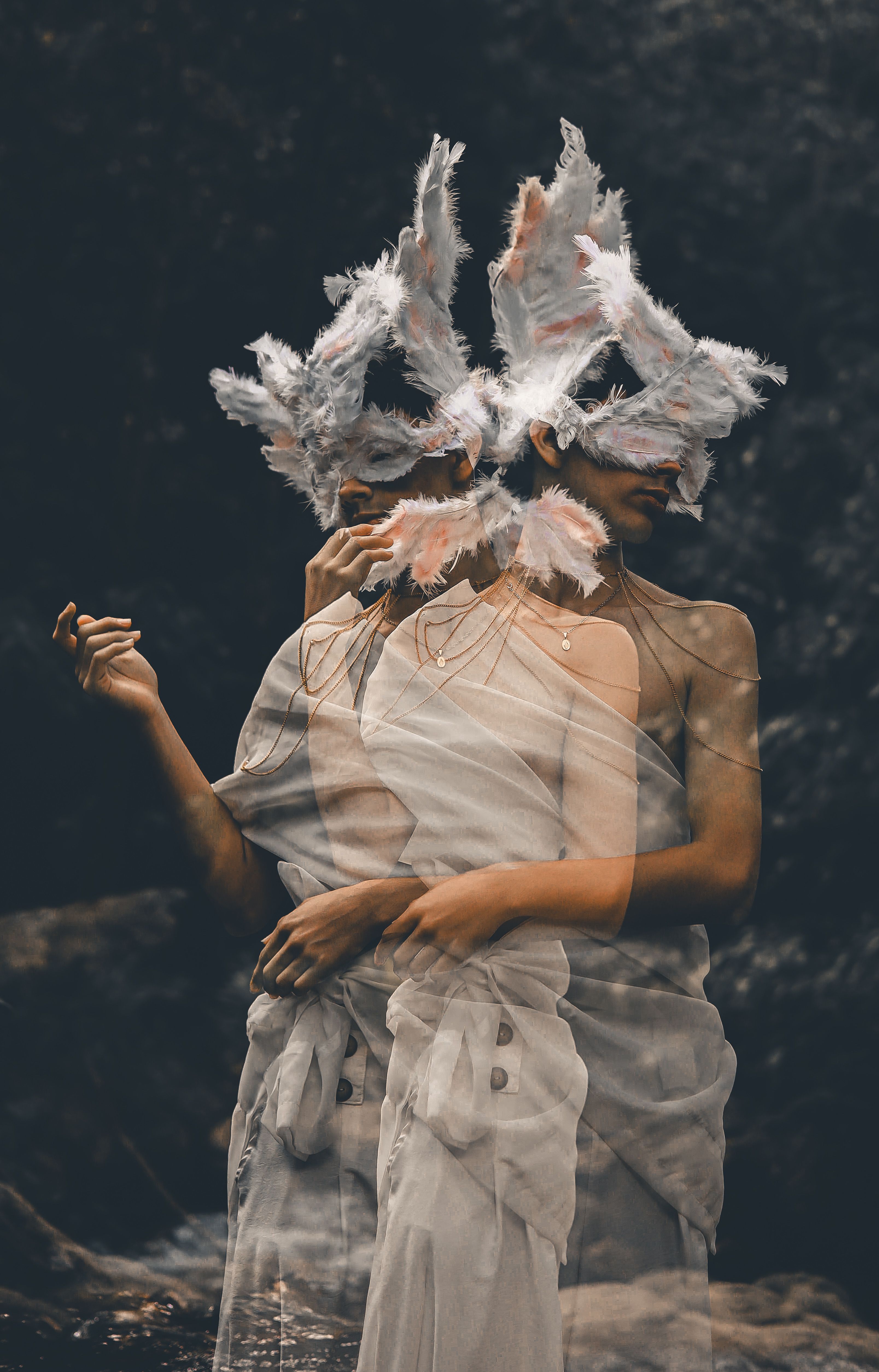 Surreal image of a woman in a feathered mask and white dress with double exposure effect.