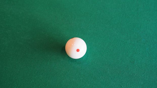 A solitary cue ball resting on a green billiard table with a red dot.