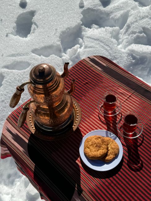 Copper teapot and glasses of tea on snowy outdoor setup with cookies.
