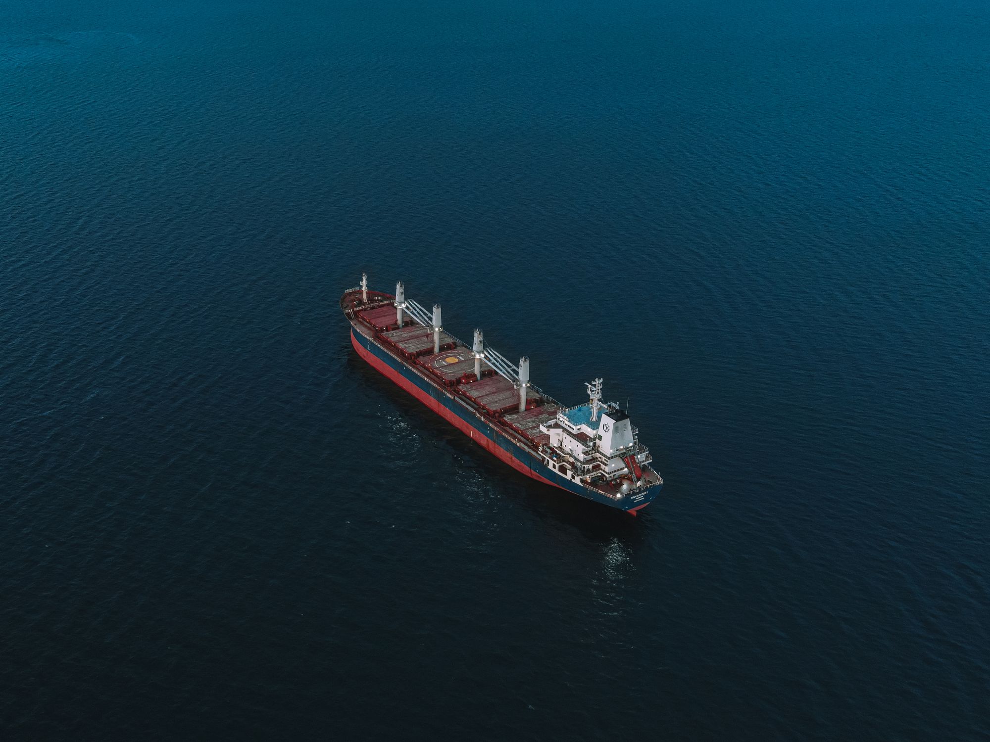 Aerial view of a cargo ship alone on a deep blue sea at dusk