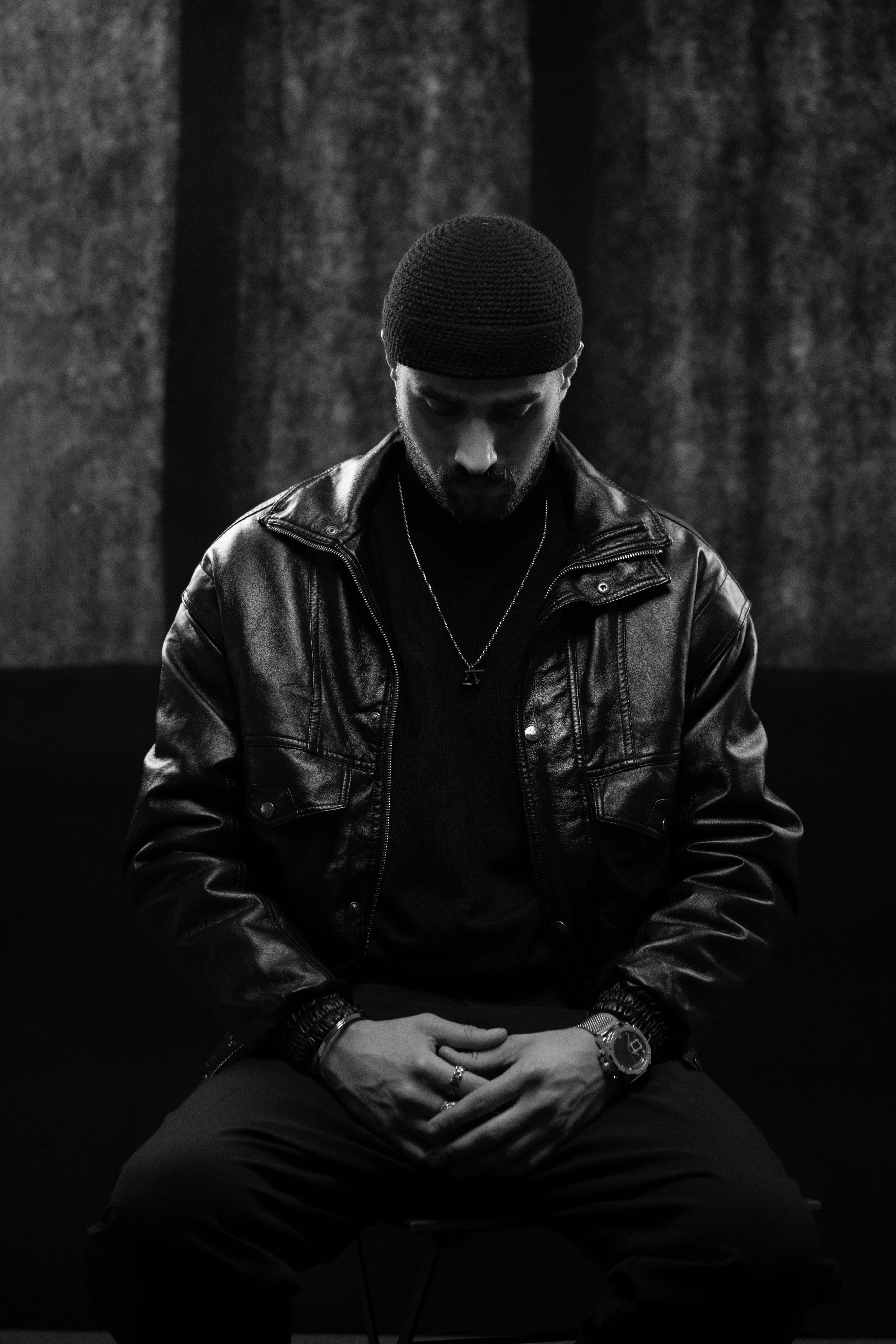 Black and white portrait of a man in a leather jacket, sitting contemplatively.