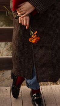 A person in fall fashion holding marigolds at a wooden railing.