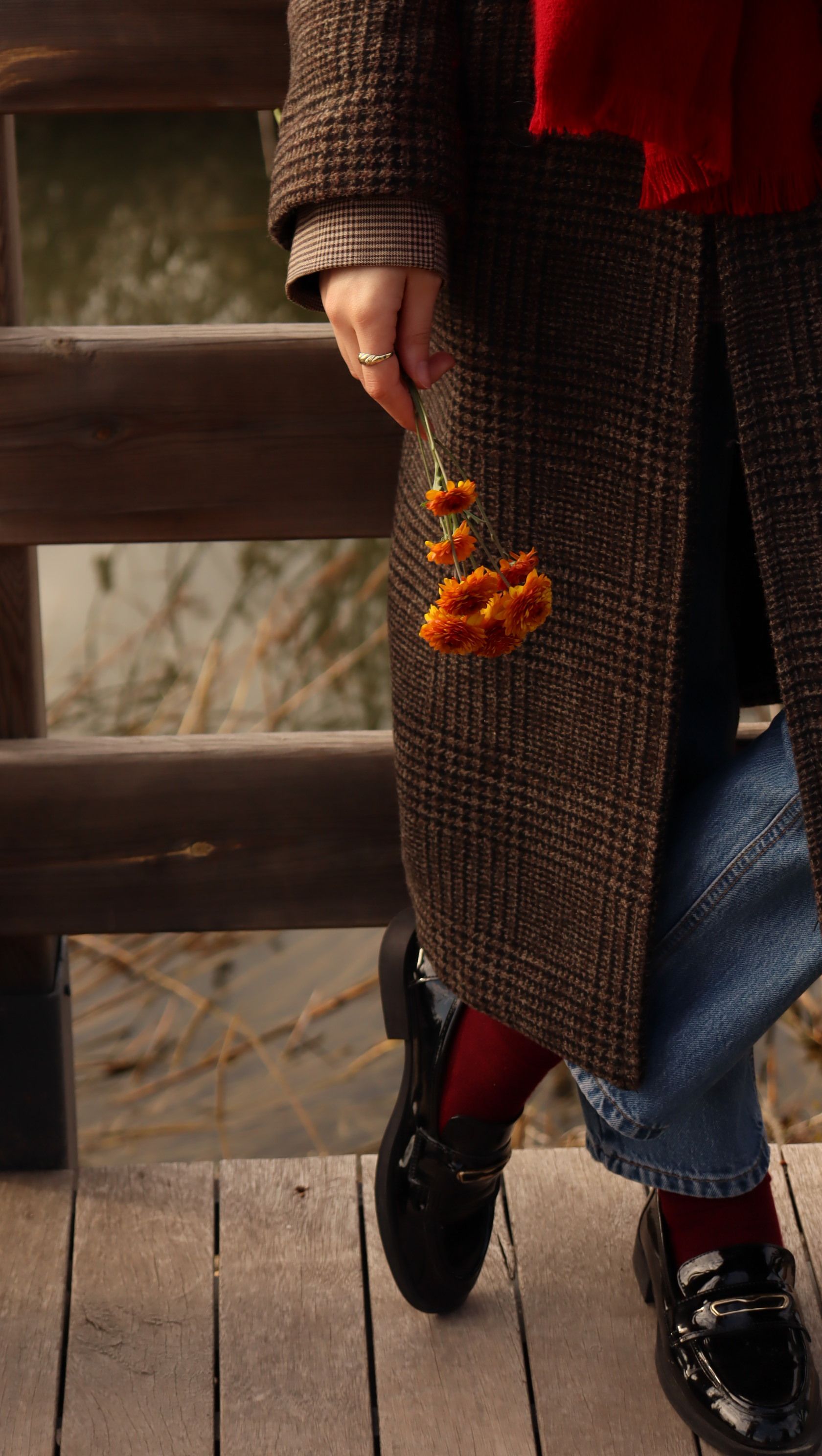 Person in warm coat with vibrant flowers enjoys a peaceful lakeside walk in the fall.