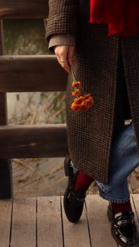 Person in warm coat with vibrant flowers enjoys a peaceful lakeside walk in the fall.