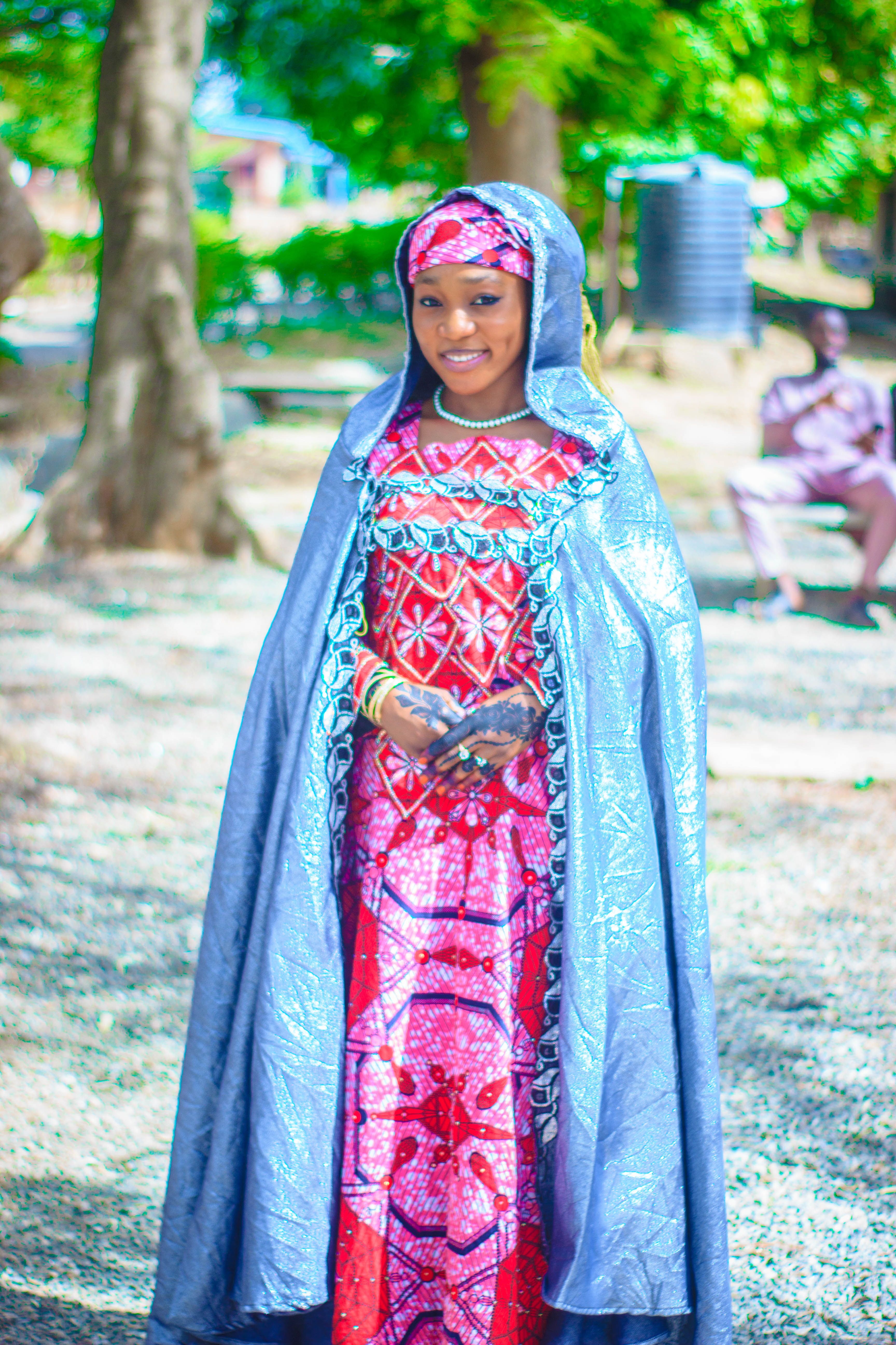 A woman in vibrant traditional African attire poses gracefully in an outdoor setting.