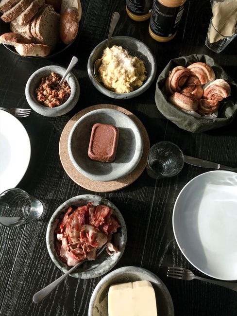 A diverse breakfast spread on a dark wooden table featuring meat, bread, and cheese.