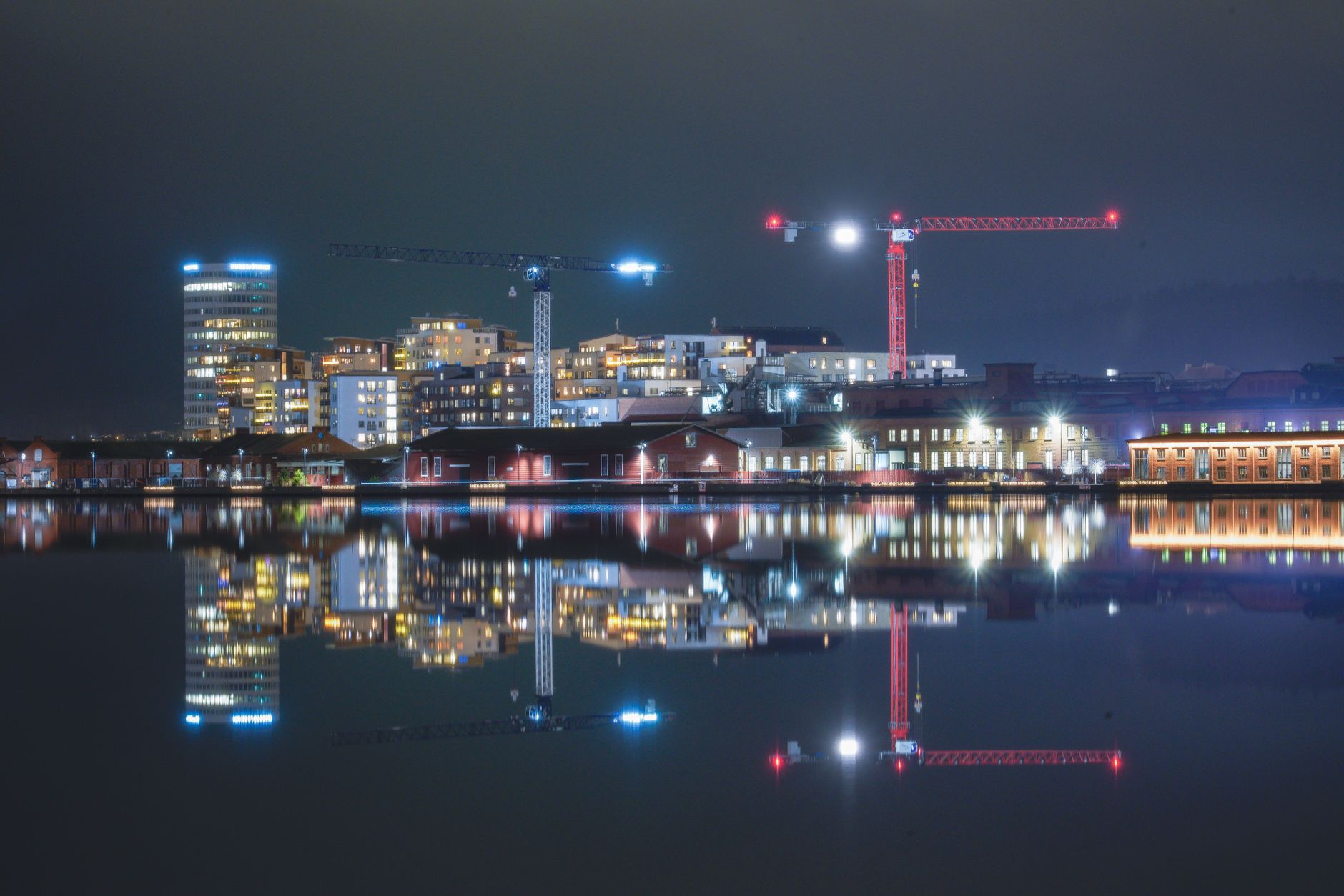 Beautiful night cityscape reflecting in water with urban lights and cranes in Jönköping, Sweden.