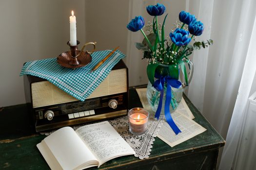 Cozy vintage setup with radio, candle, open book, and blue tulips in vase.