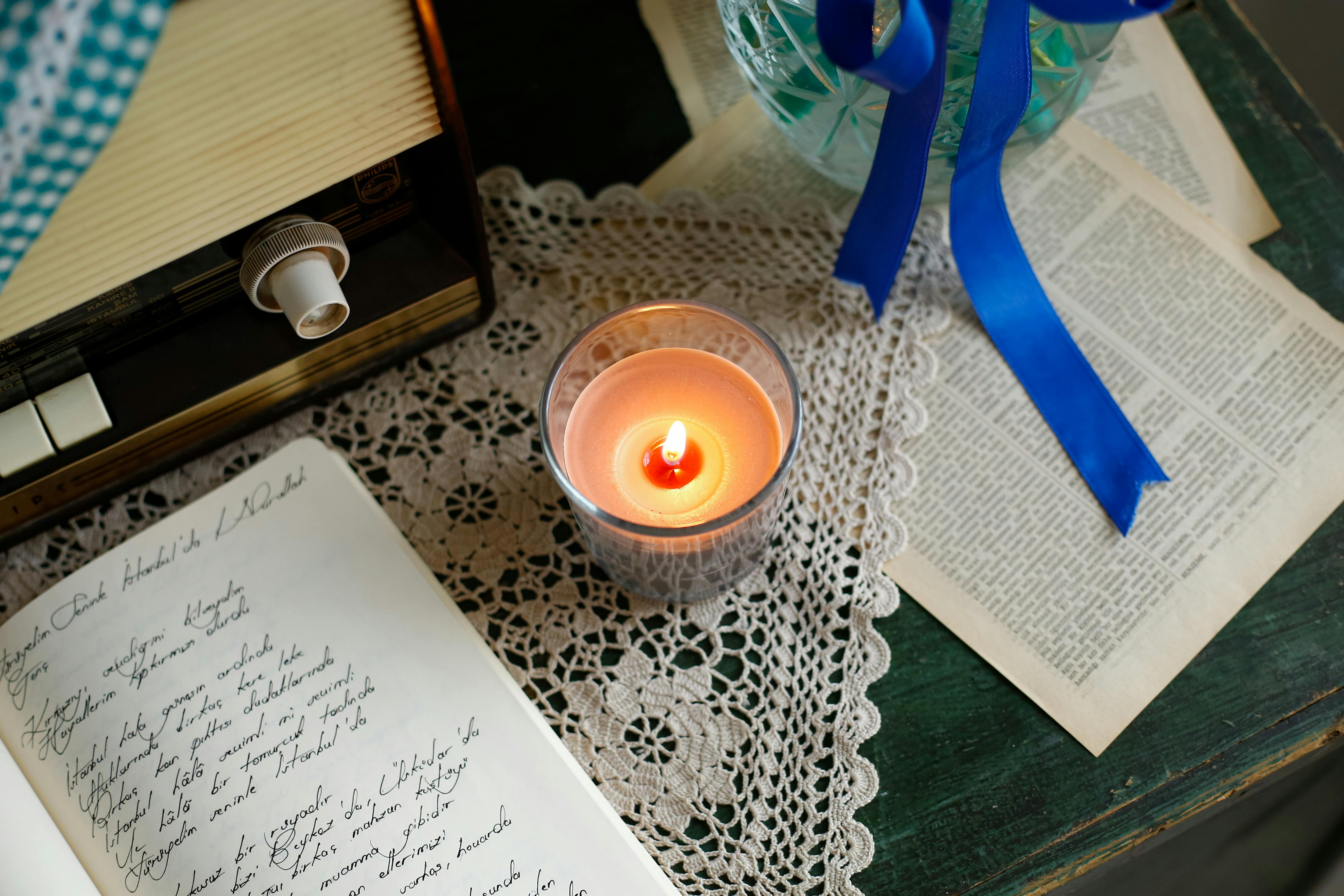 A cozy flat lay featuring a candle, vintage radio, handwritten journal, and crochet cloth.