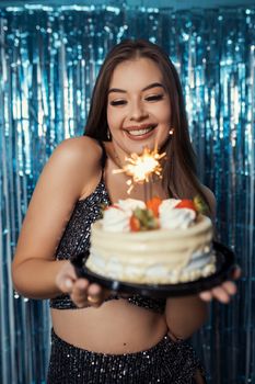 Happy young woman celebrating her birthday with a sparkling cake and a radiant smile.