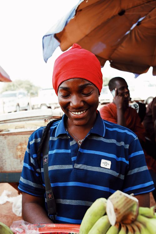Free African street vendor smiling while selling fresh produce in Abuja market. Stock Photo