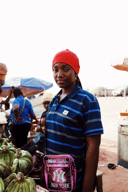 Free Portrait of a young woman with a red headscarf at an open market in Abuja, Nigeria, selling plantains. Stock Photo