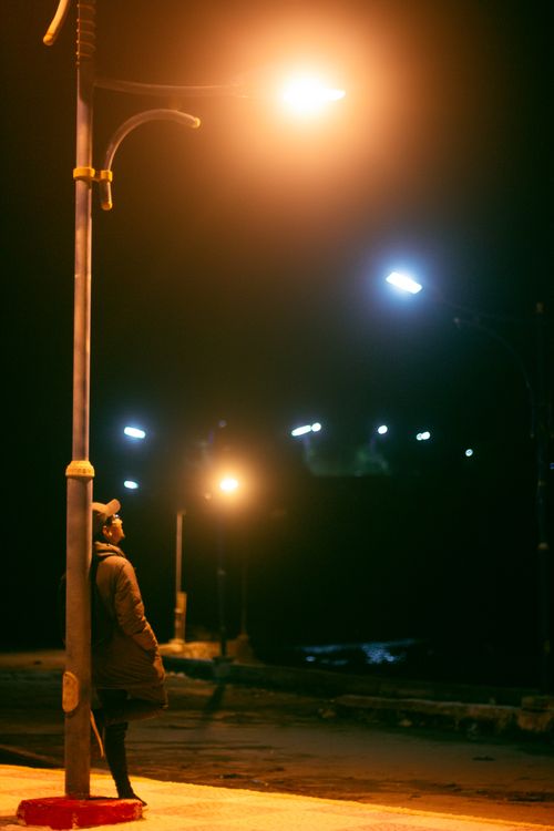 Free A person leans on a streetlight in Collo, Algeria, illuminated by warm night lighting. Stock Photo