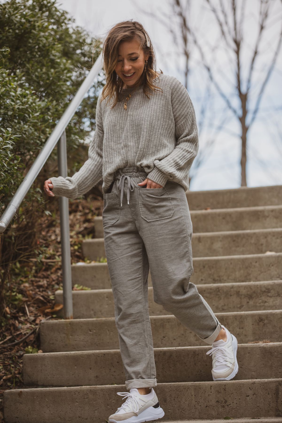 Woman in casual gray outfit walks down outdoor steps with trees in background.