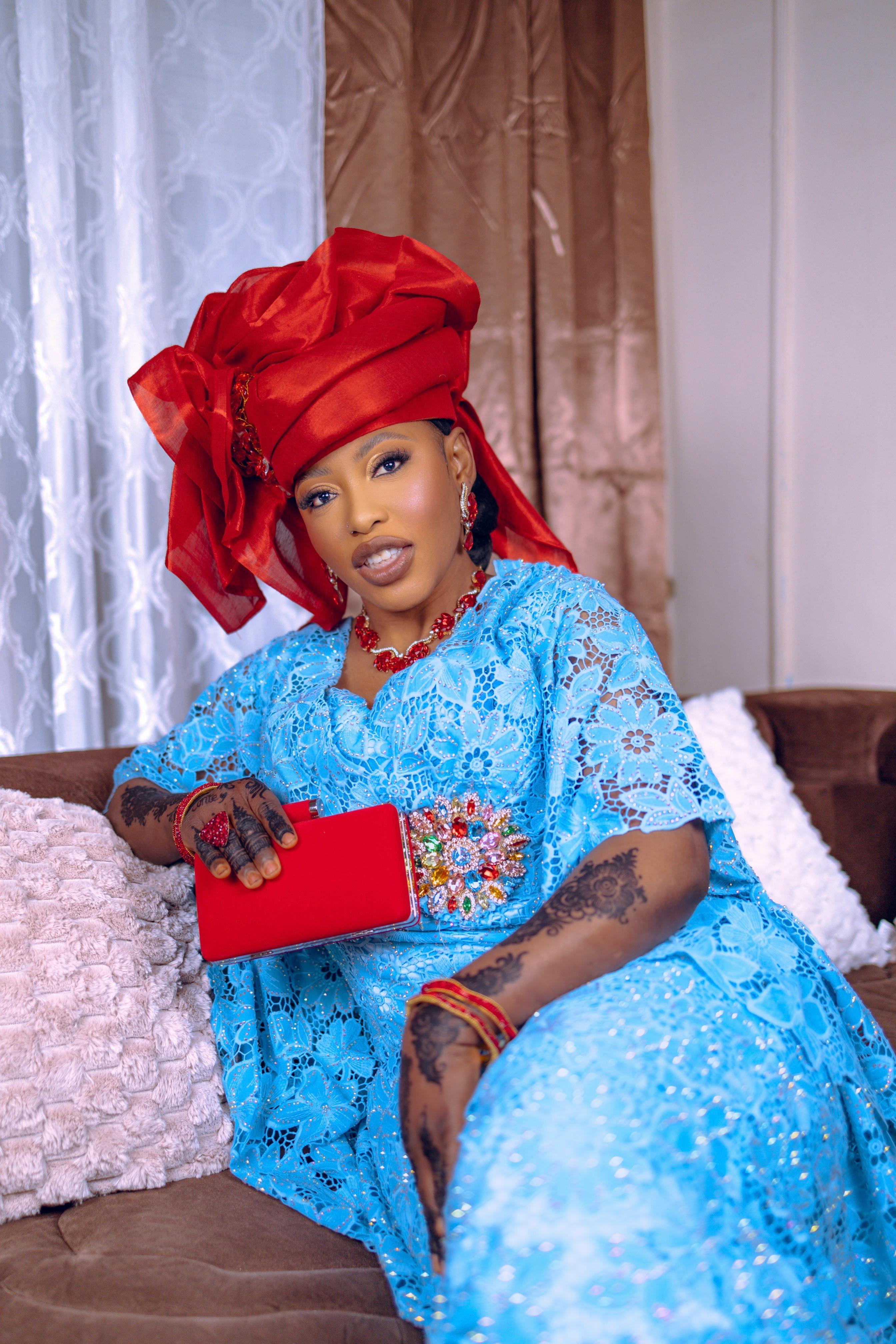 Kostenlos Frau in farbenfroher nigerianischer Kleidung mit rotem Kopftuch und blauem Kleid, im Haus. Stock-Foto