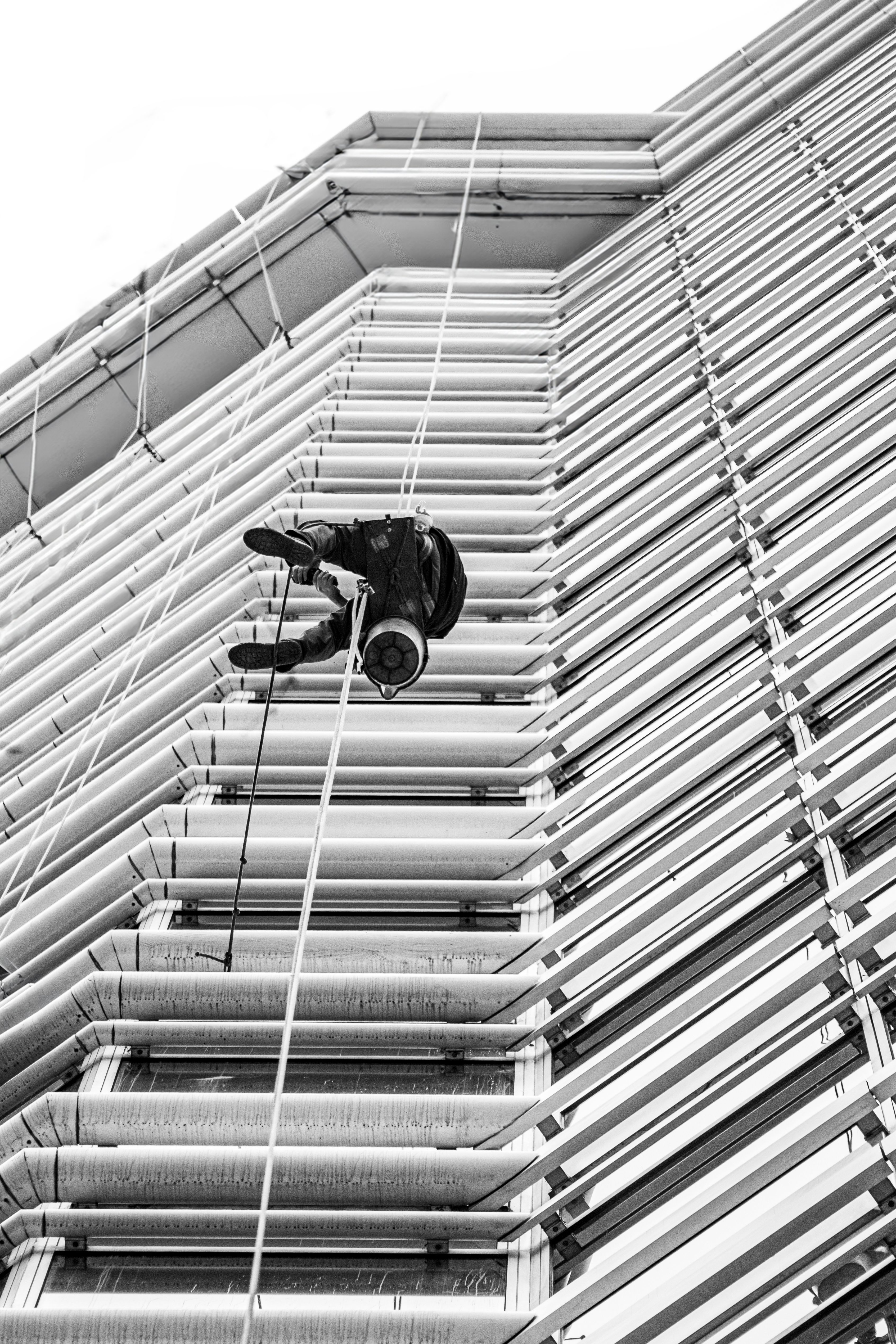 A monochrome view of a high-rise worker suspended on the side of a building in Buenos Aires.