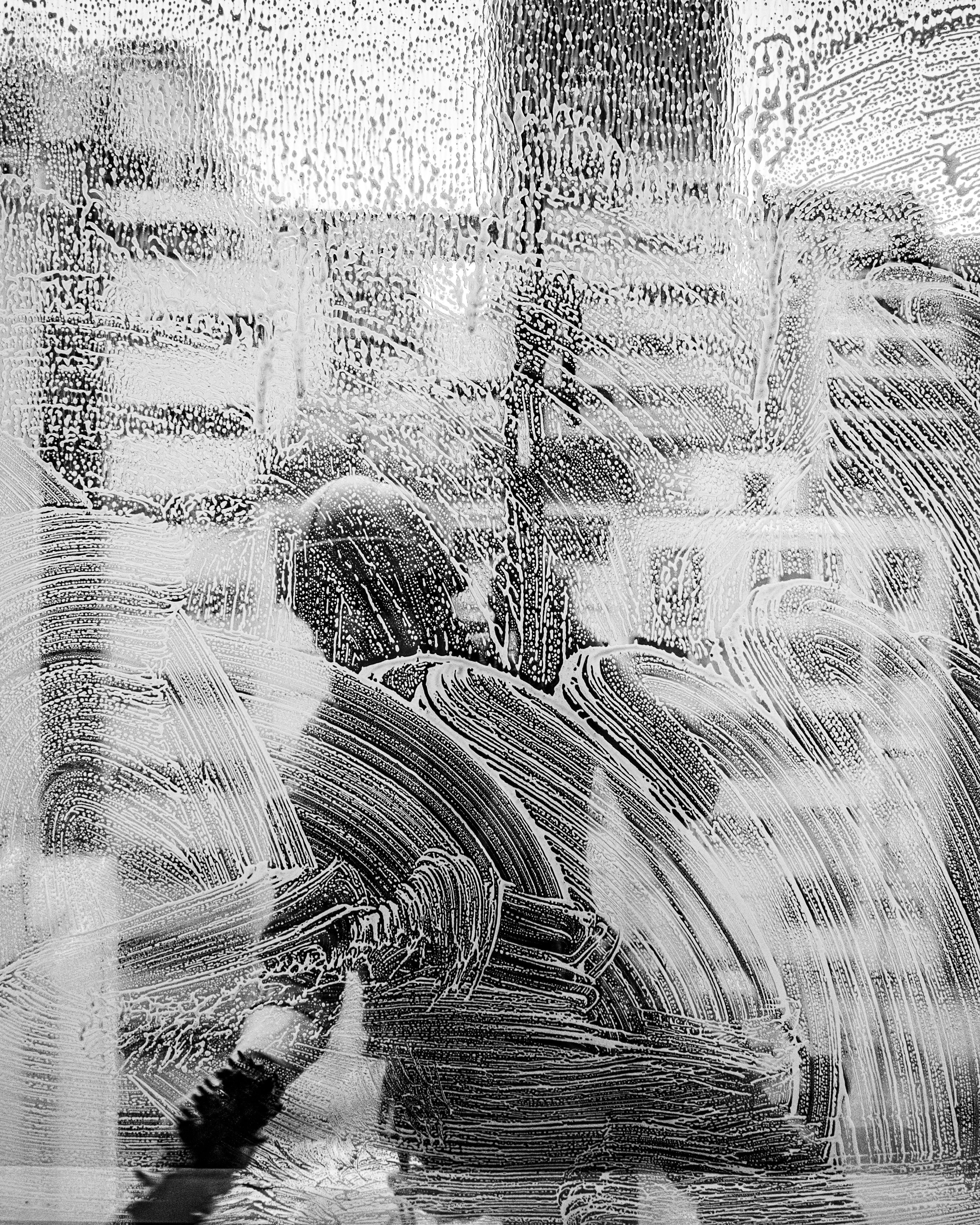 grátis Uma cena urbana em preto e branco vista através de um vidro embaçado, capturando a essência da vida na cidade. Foto profissional