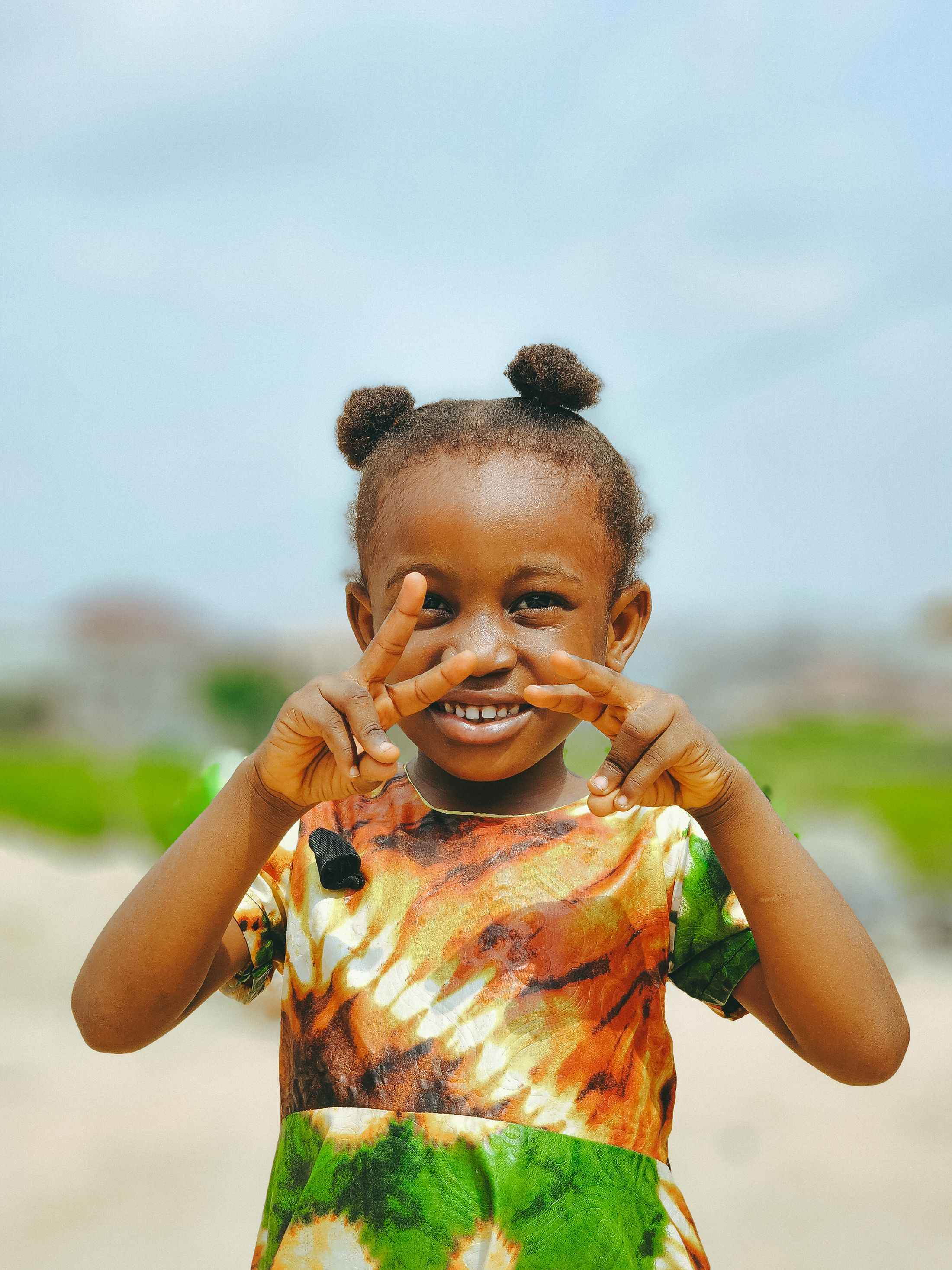 A young girl outdoors in Lagos, hair in two puffs, looking straight at the camera.
