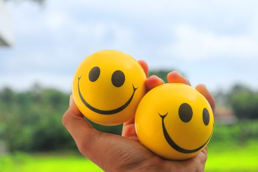 Two yellow smiley face balls in a hand against a vibrant outdoor background.
