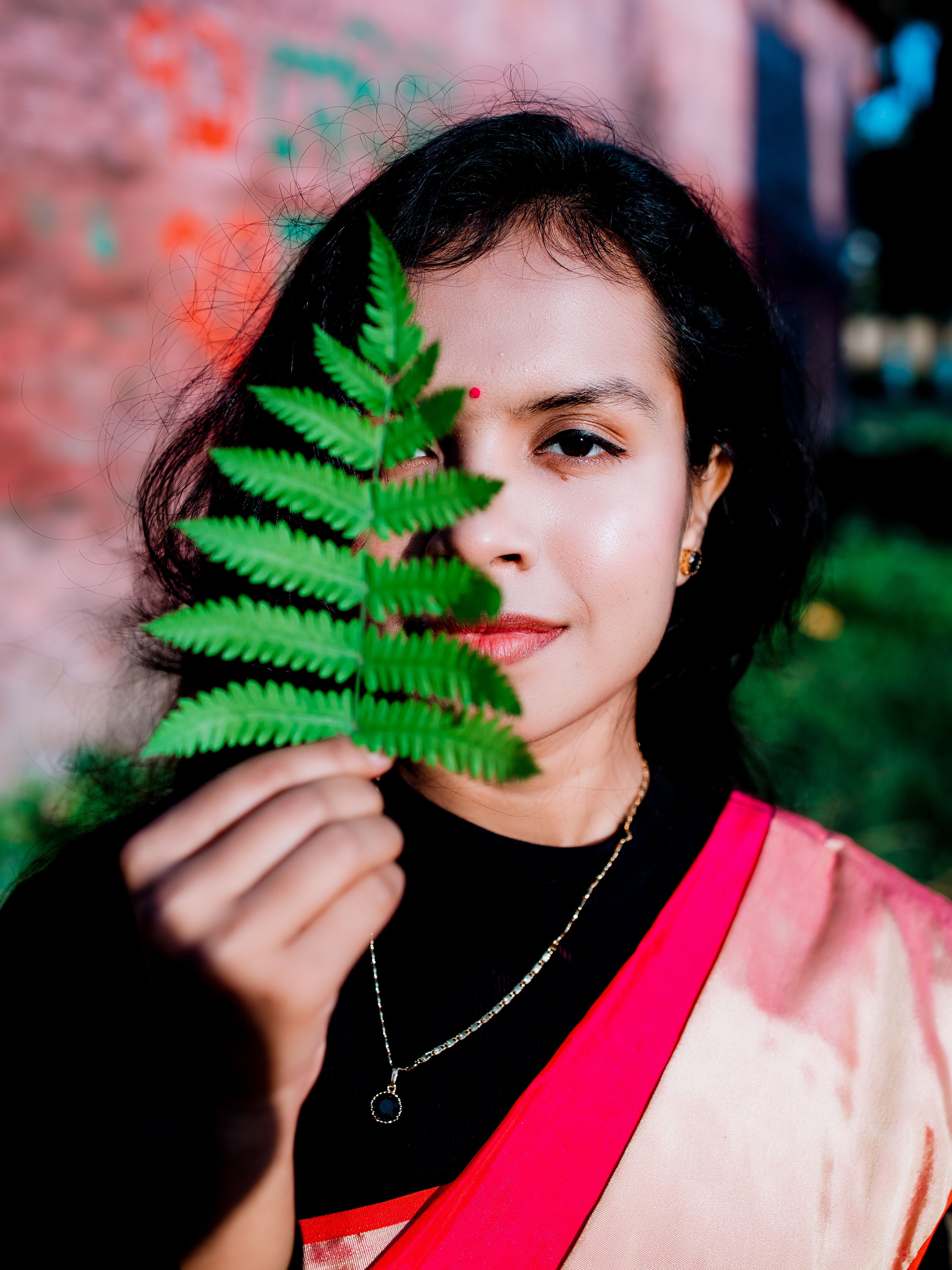 Portrait of a young woman in traditional dress holding a green fern leaf on a sunny day.
