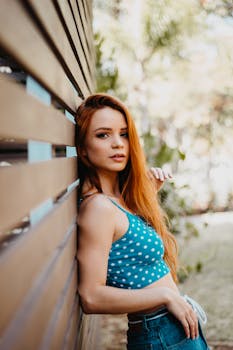 一位红发迷人的女子身着圆点上衣，倚靠在木墙上摆姿势