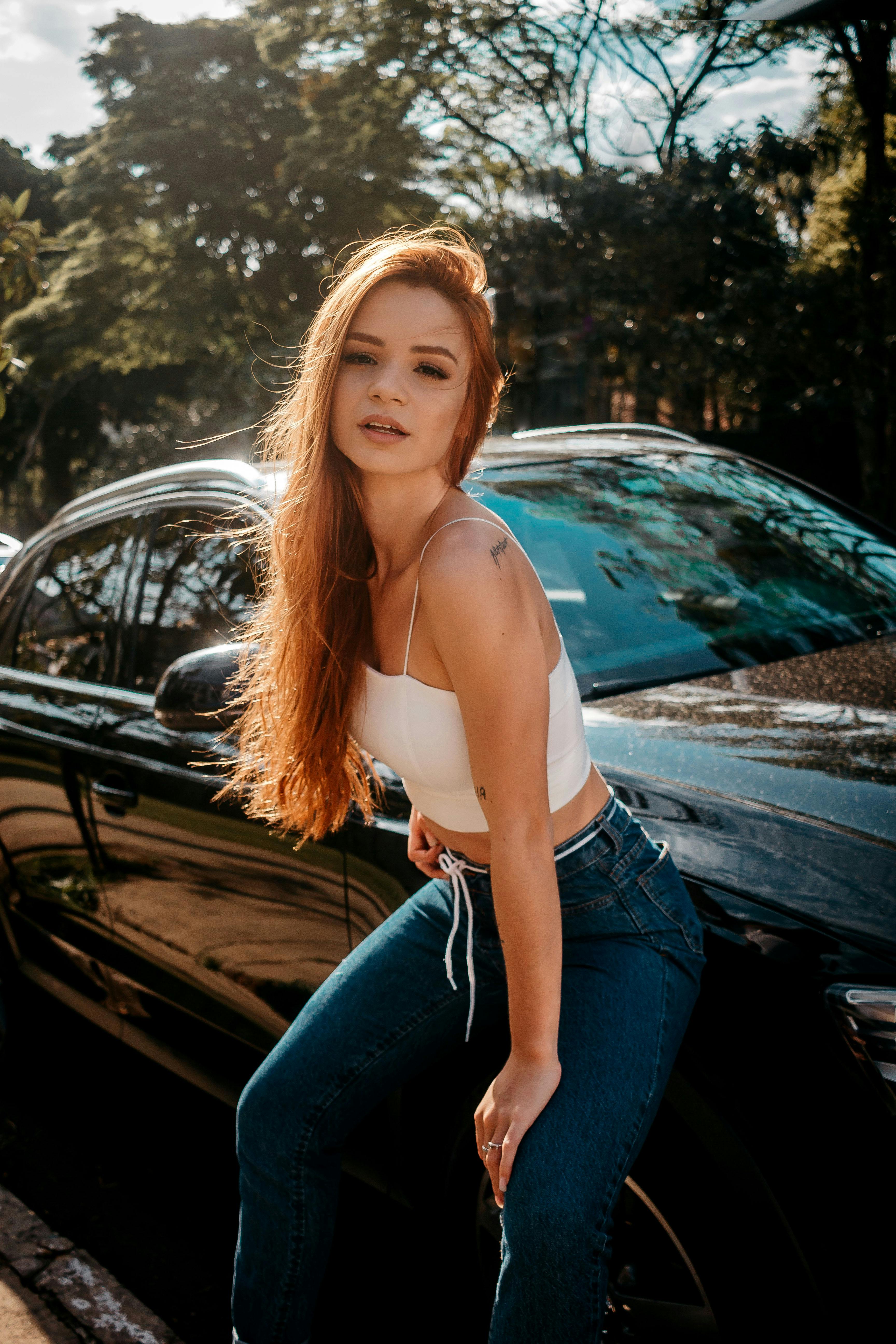 白天，一位红发时尚女子自信地在一辆时髦的汽车旁摆出姿势