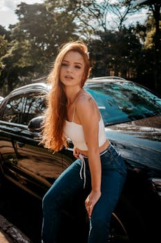 白天，一位红发时尚女子自信地在一辆时髦的汽车旁摆出姿势
