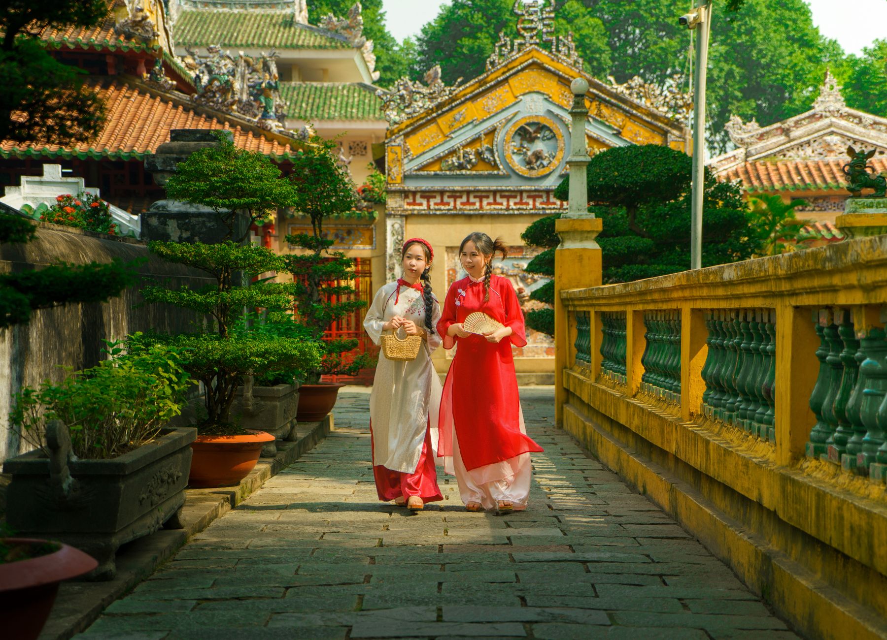 Two Vietnamese women in ao dai walk through a historic temple in Ho Chi Minh. Vibrant colors highlight cultural heritage