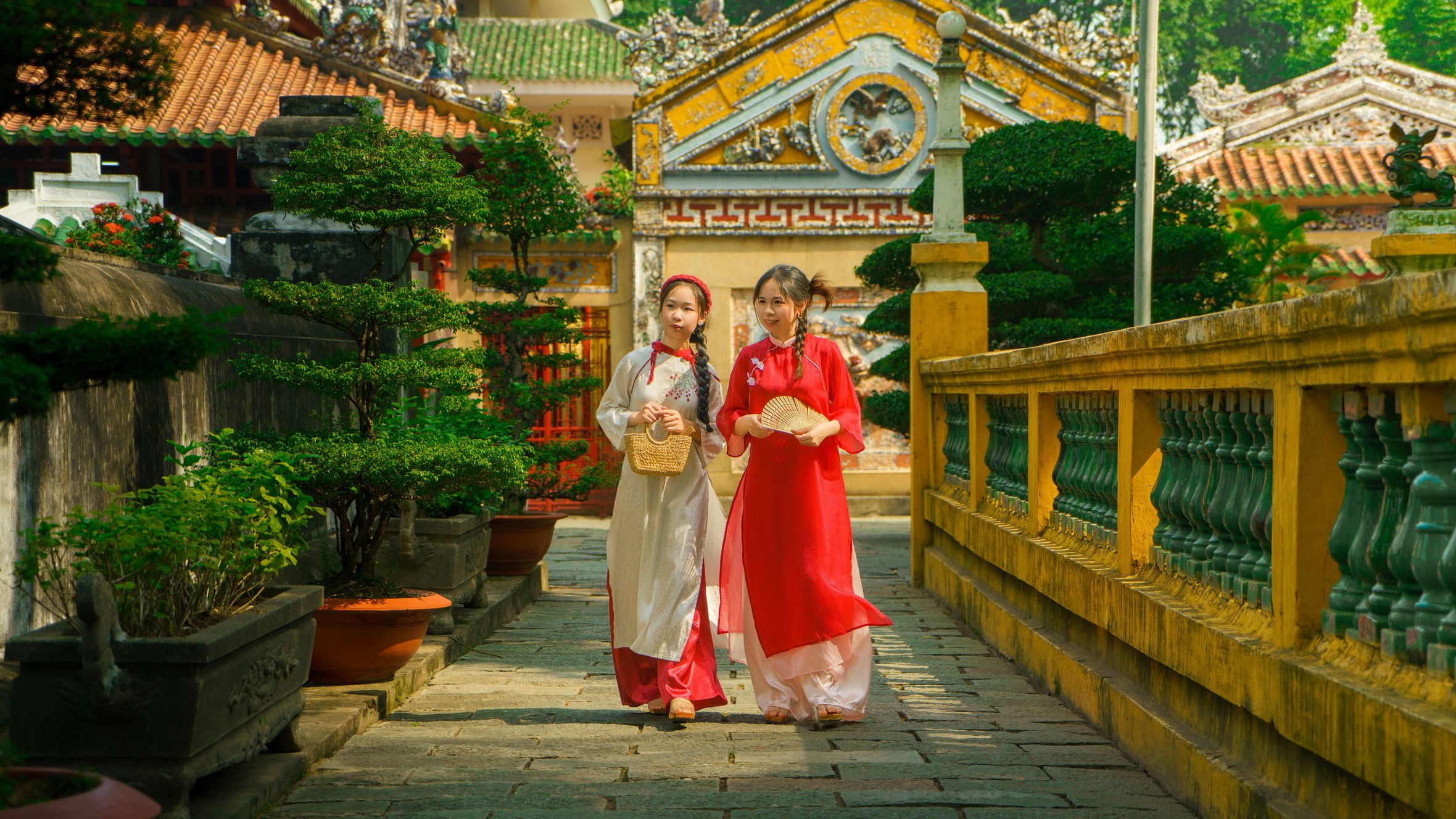 Two Vietnamese women in ao dai walk through a historic temple in Ho Chi Minh. Vibrant colors highlight cultural heritage.
