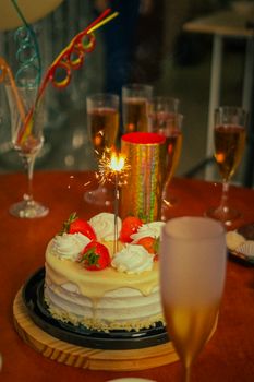 A celebration with a cake topped with a sparkler, surrounded by champagne glasses, creating a festive ambiance.