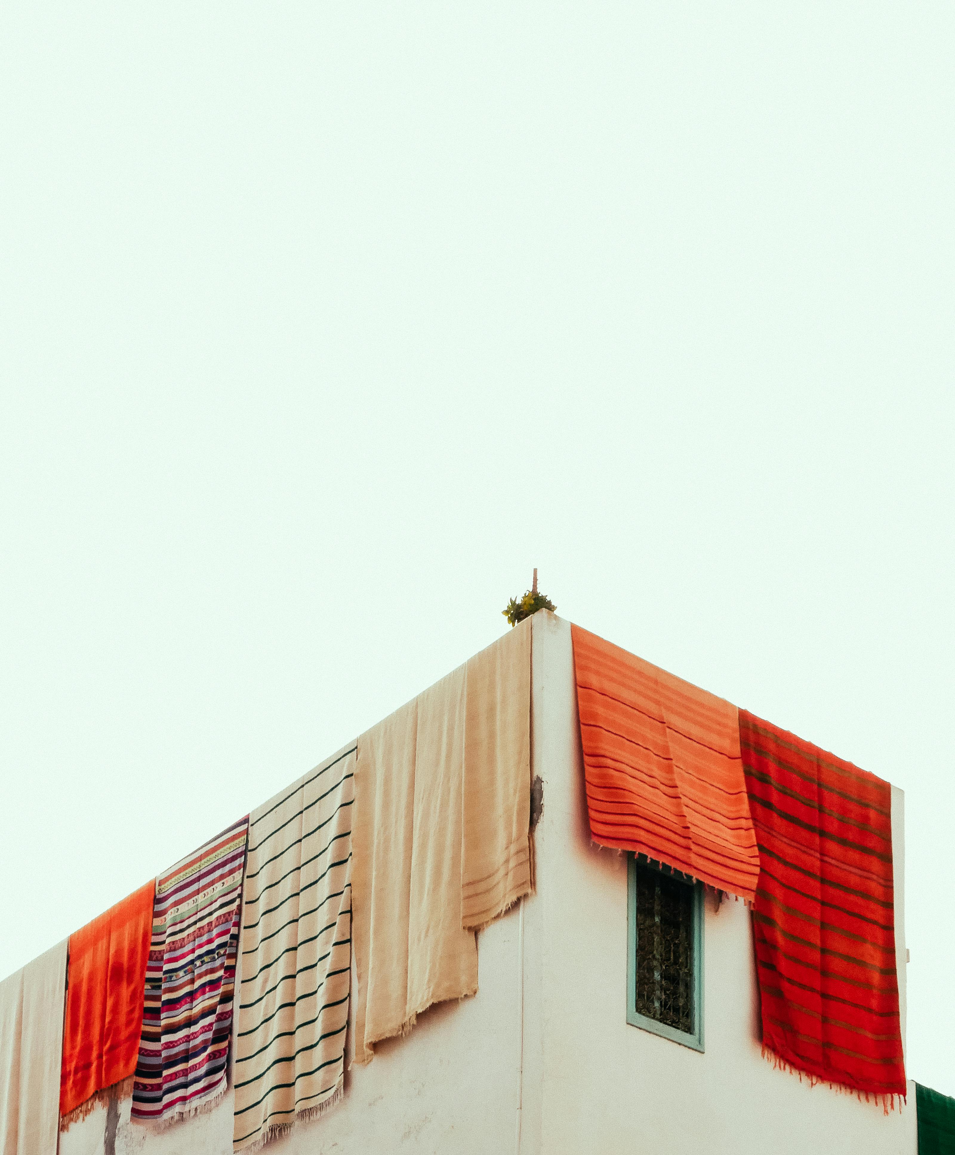 Gratis Farverige marokkanske tæpper hængende til tørre på et Asilah-tag under en klar himmel. Lagerfoto