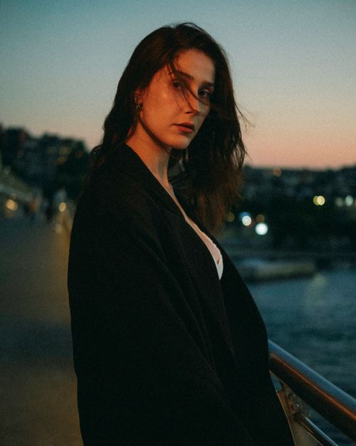 Free Moody portrait of a woman at twilight by the sea with a vibrant sunset background. Stock Photo