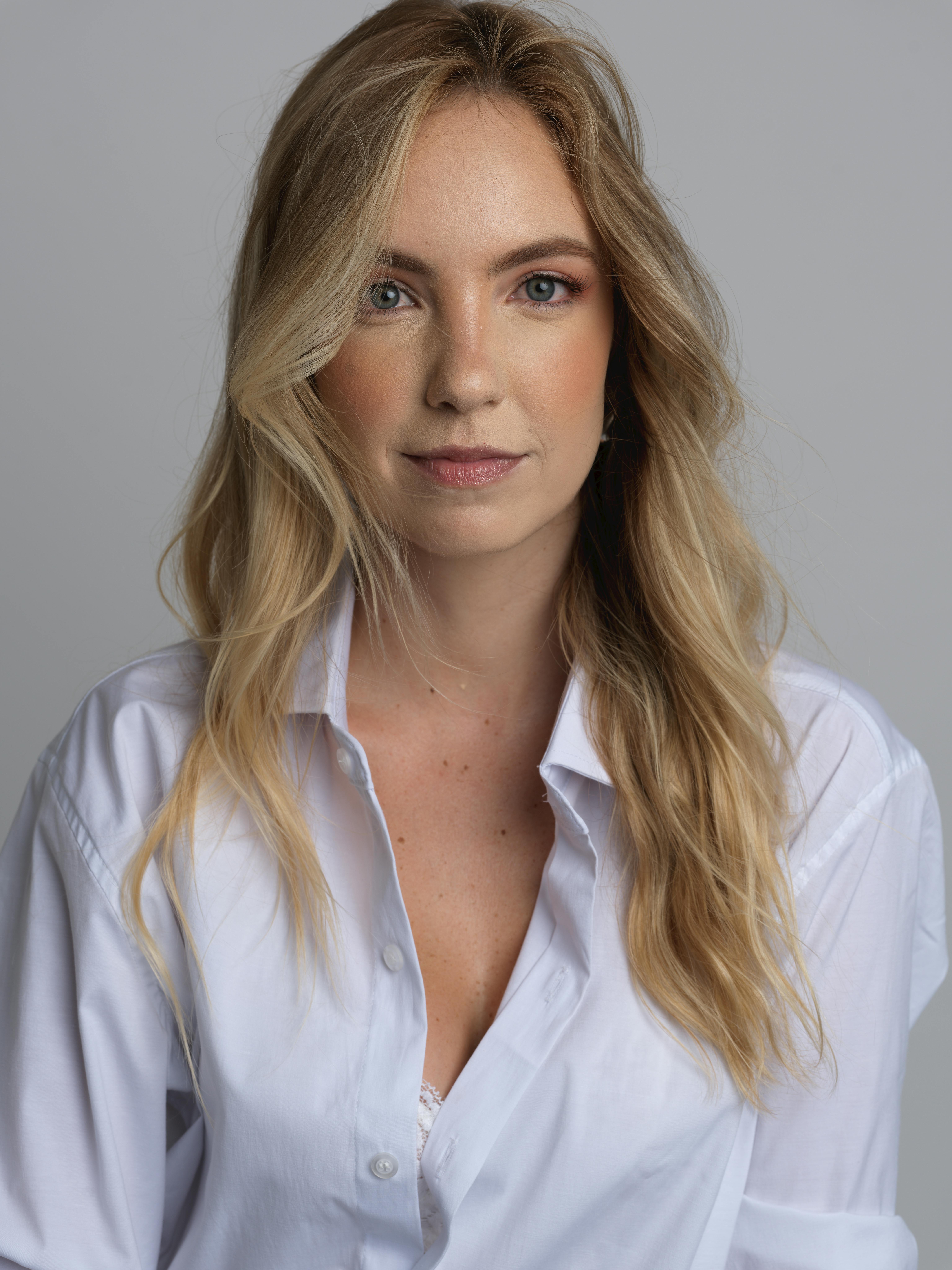 Elegant portrait of a blonde woman in a white shirt, set against a neutral background.