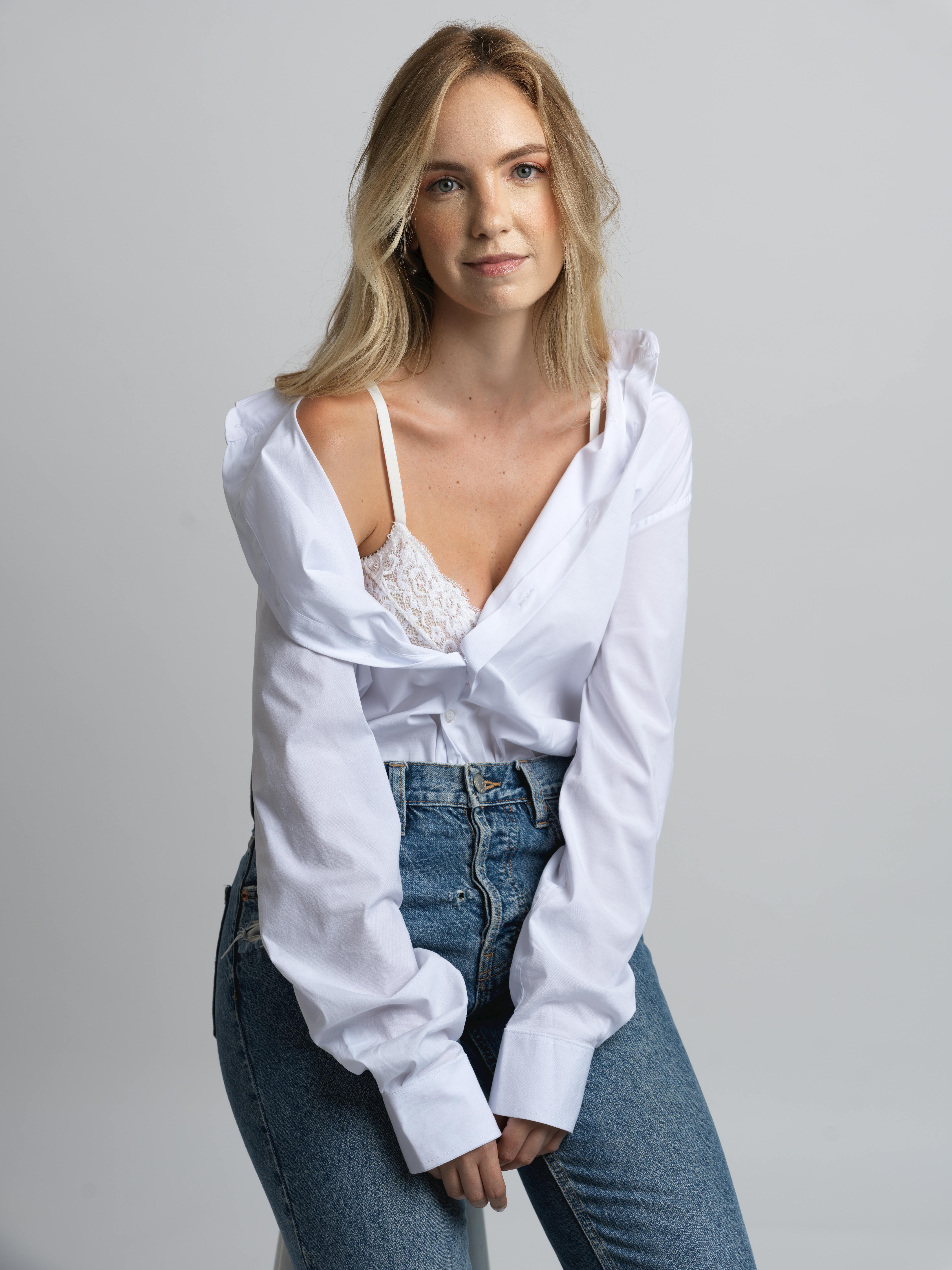 Young woman in white shirt and jeans poses confidently indoors.