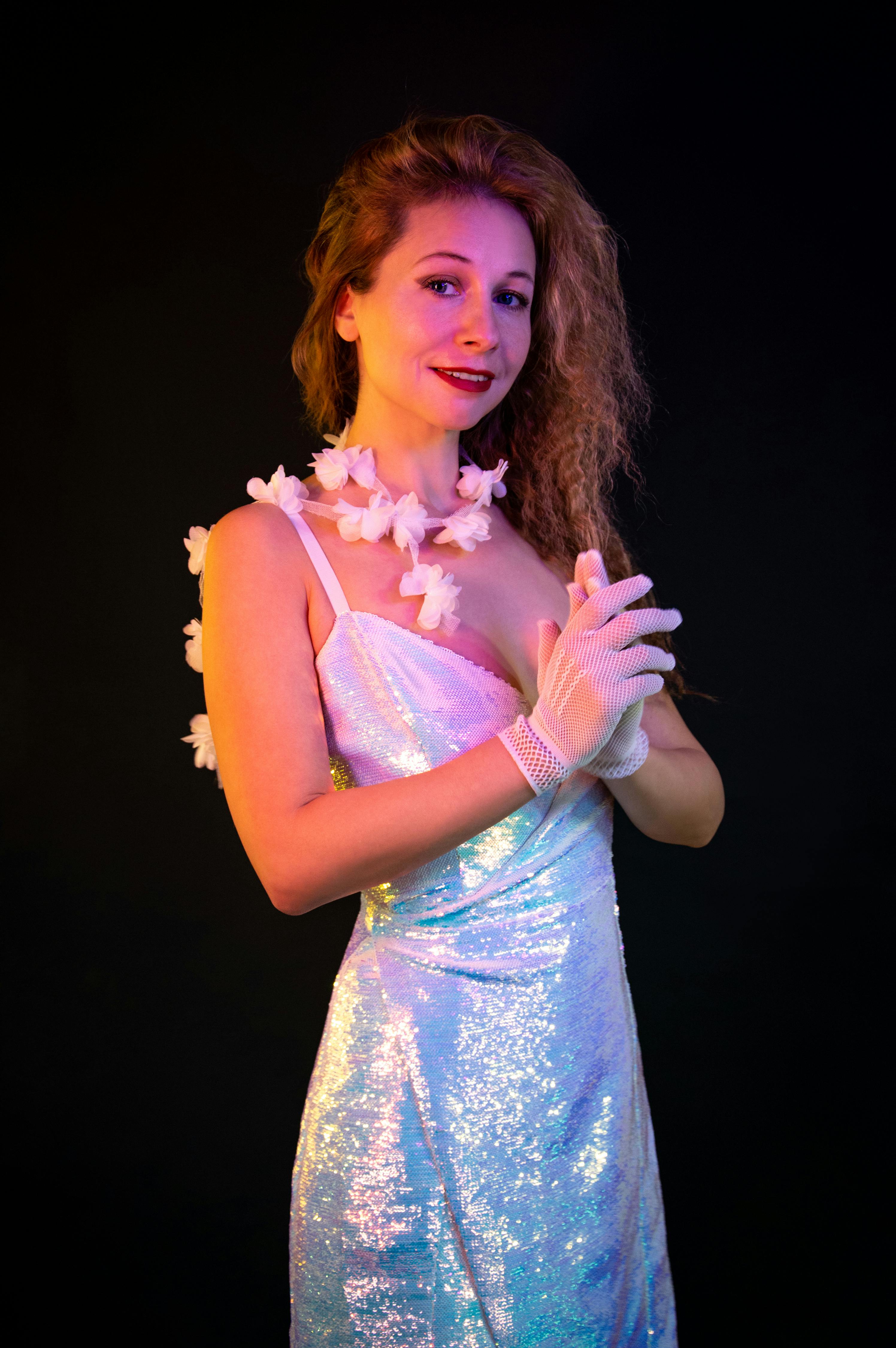 Kostnadsfria Porträtt av en kvinna i en skimrande klänning med blommiga accessoarer, mot en mörk bakgrund. Stock foto