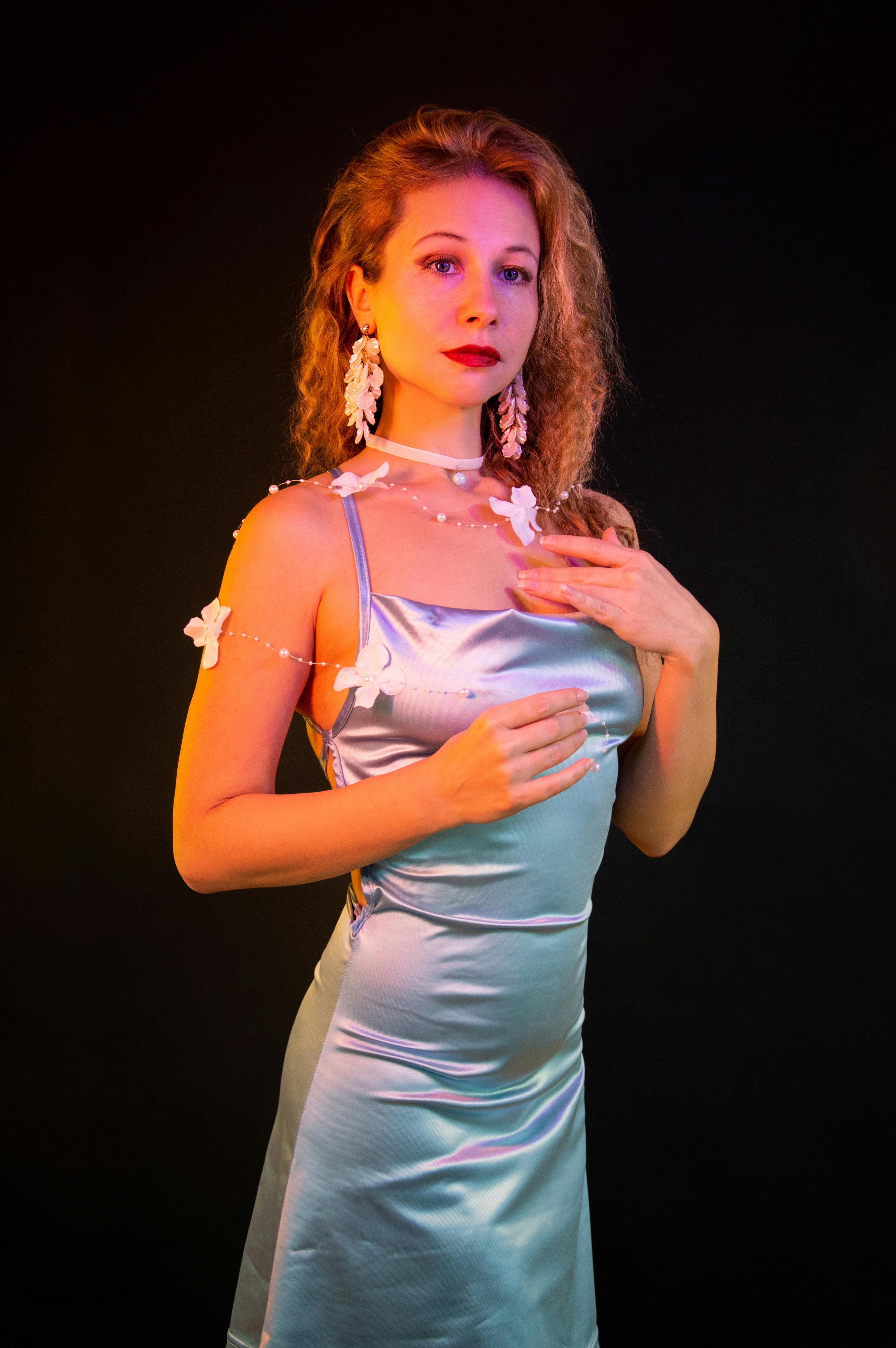 Gratuit Une femme vêtue d'une robe en satin pose élégamment sous un éclairage vibrant, mettant en valeur la mode et le style. Photos