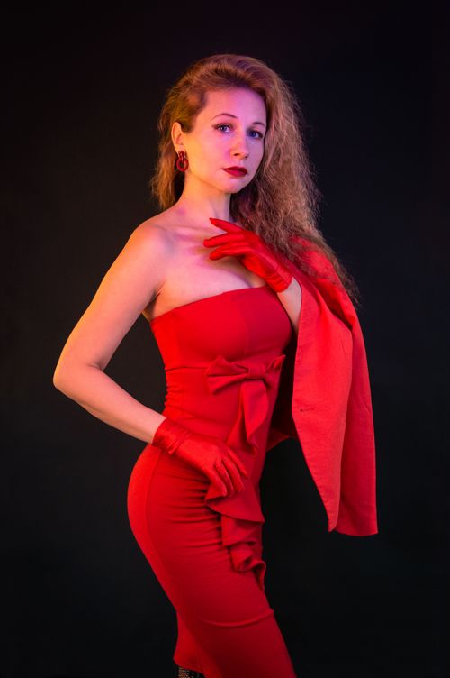 Free Stylish woman in a red dress posing gracefully against a dark background. Stock Photo