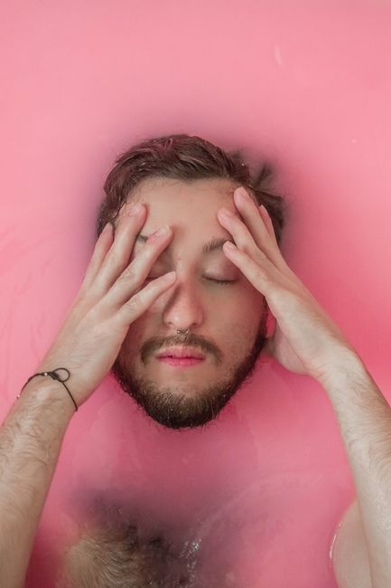 Young man relaxing with eyes closed in pink water, showcasing tranquility and introspection.