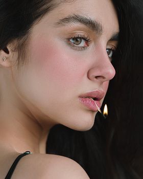 Close-up portrait of a woman with a matchstick lit, capturing intensity and emotion.