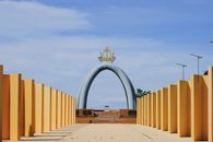 A grand architectural scene with a golden archway and lined yellow columns under a blue sky.