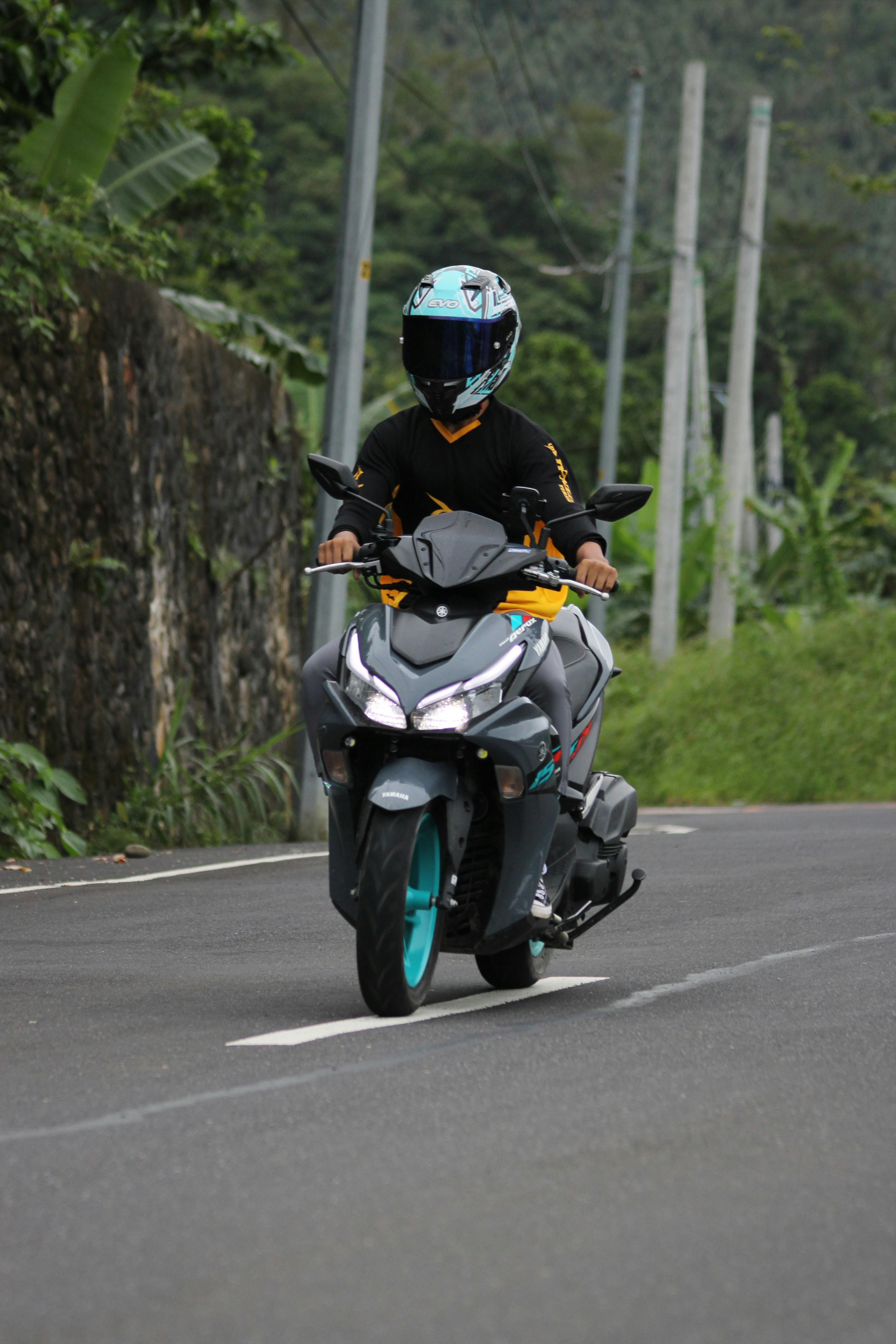 A motorcyclist with helmet rides down a scenic country road surrounded by greenery.