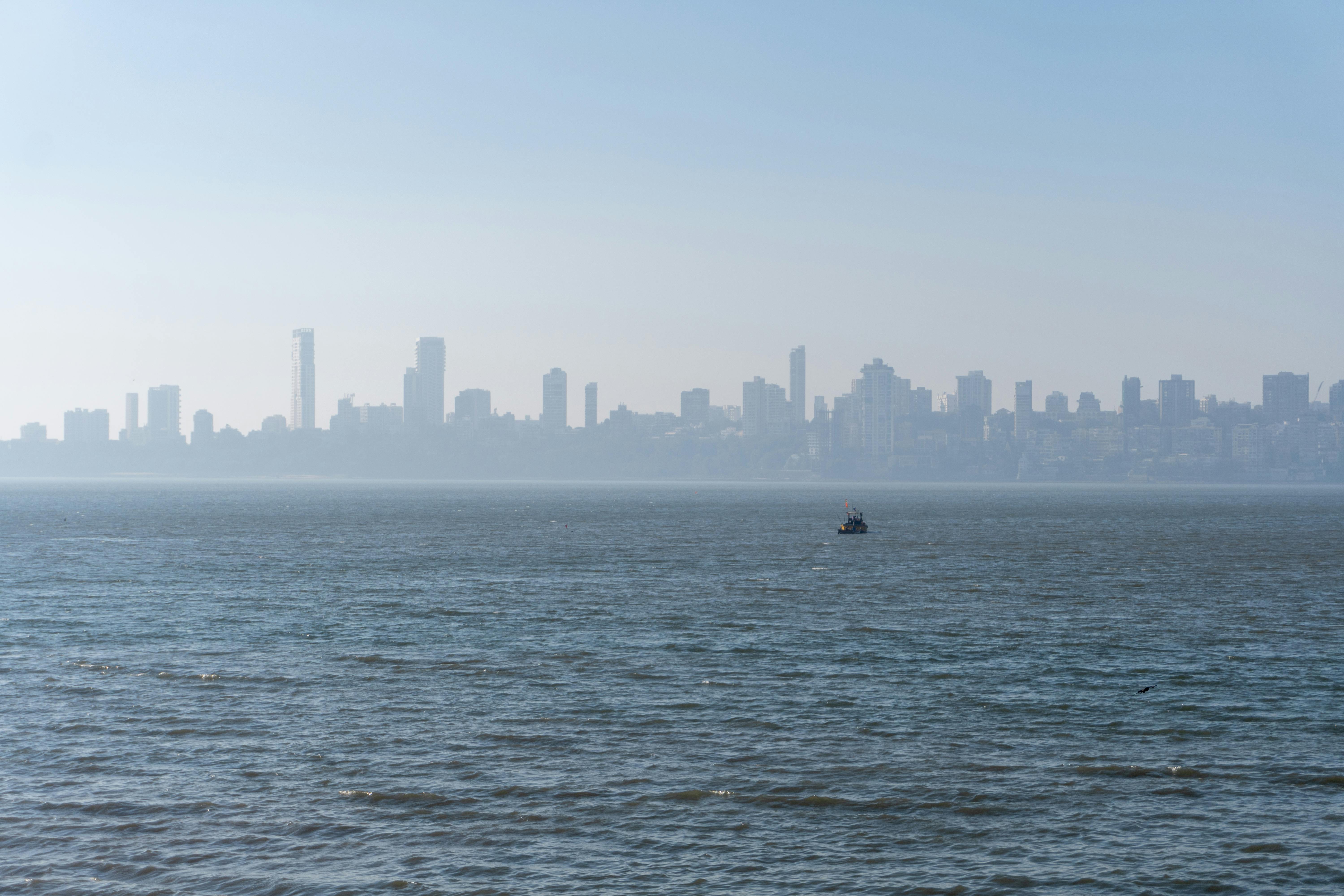 Calm sea with a distant view of Mumbai's modern skyline and clear blue sky.