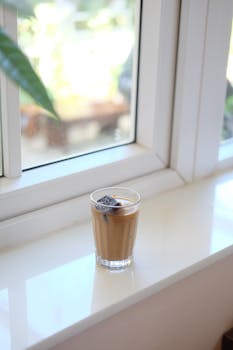 A glass of iced coffee on a sunny white windowsill, indoors during the day.