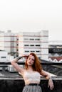 红发女子在屋顶上以城市景观为背景摆姿势，展示纹身和时尚风格