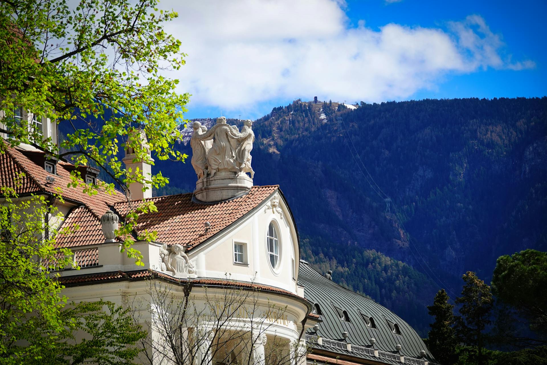 Elegant architecture in Meran, Italy with scenic mountain backdrop under a bright blue sky.