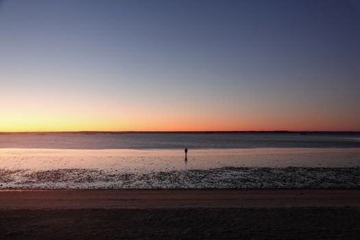 A lone person stands at Stamford beach during a serene sunrise, reflecting solitude and tranquility.