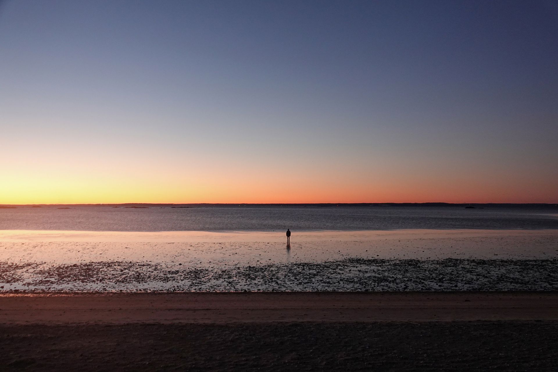A lone person stands at Stamford beach during a serene sunrise, reflecting solitude and tranquility.