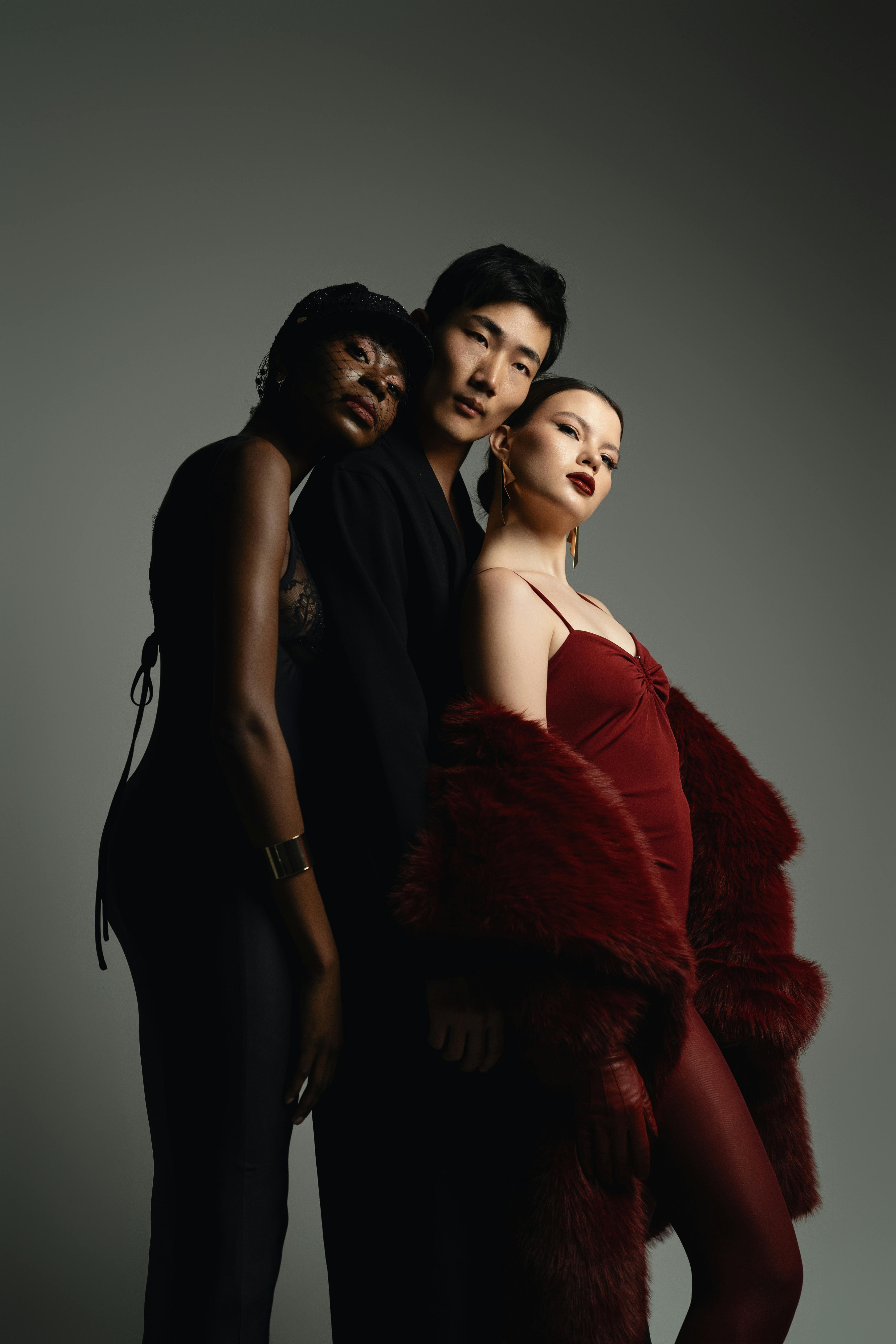 Gratis Tiga model berpose elegan di sebuah studio, memamerkan gaya busana yang beragam dan pencahayaan yang suram. Foto Stok