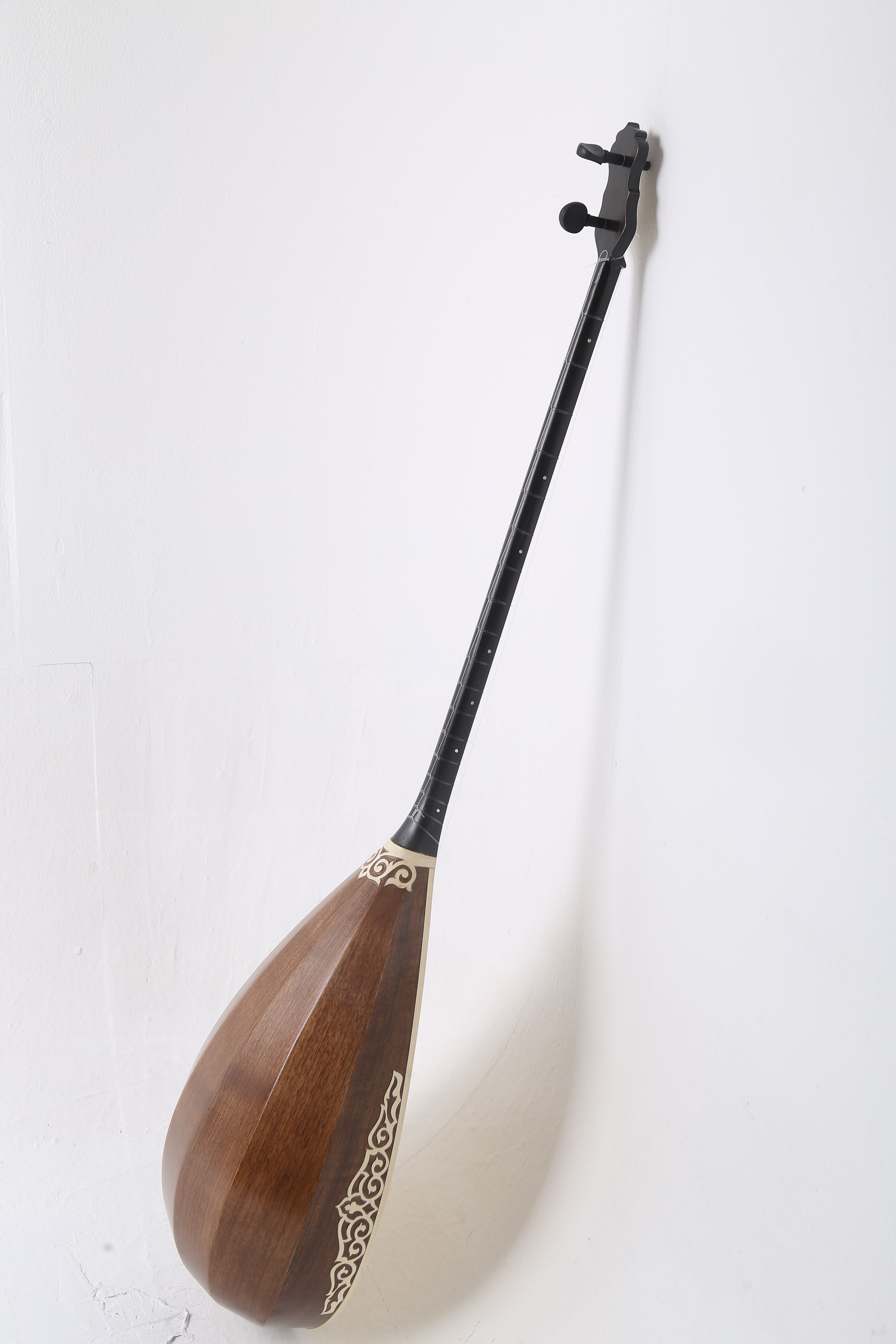 Traditional Kazakh dombyra with intricate design against a white wall.