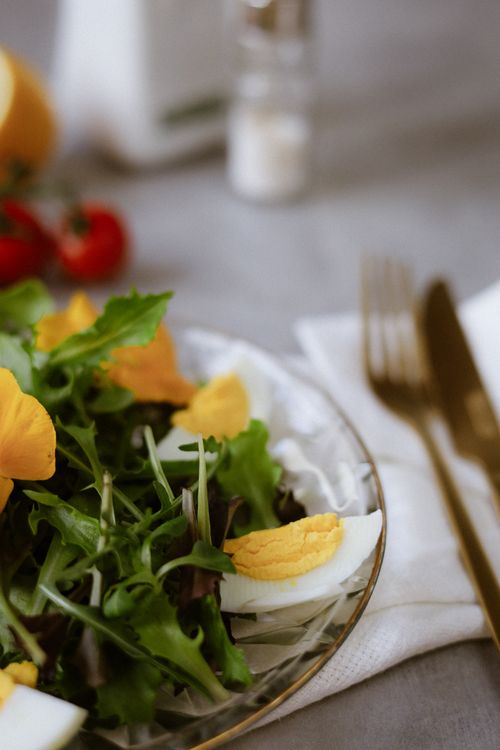 Free A vibrant salad with fresh greens, sliced eggs, and edible flowers on a glass plate. Stock Photo